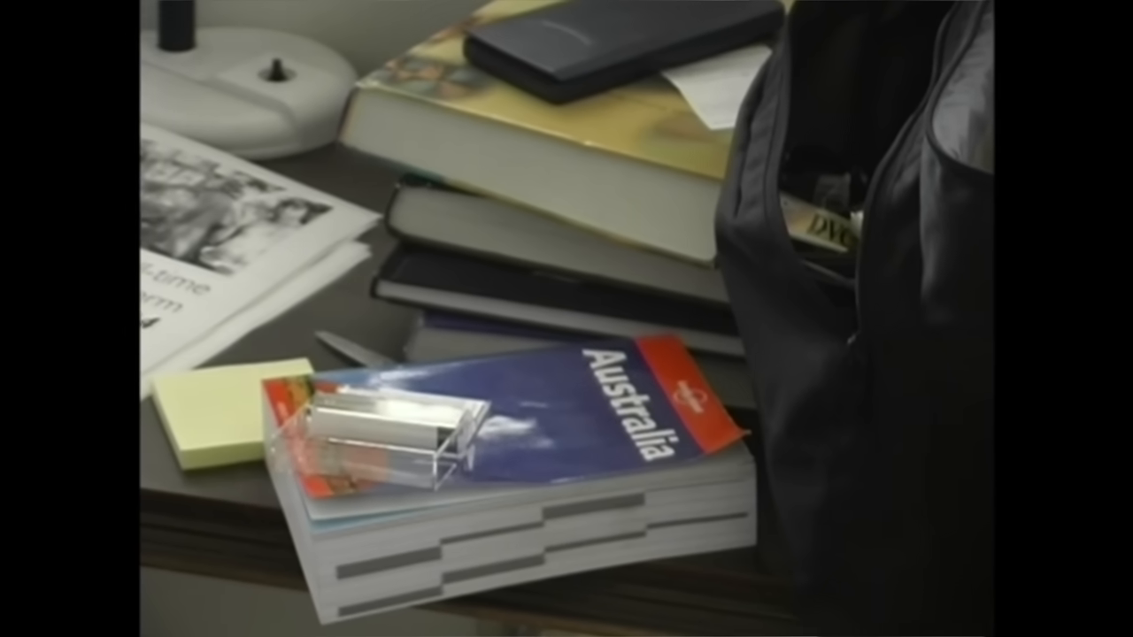 [03:54] A shot of his desk featuring the "Lonely Planet Australia" guide and a 2004 Film-time Application Form.