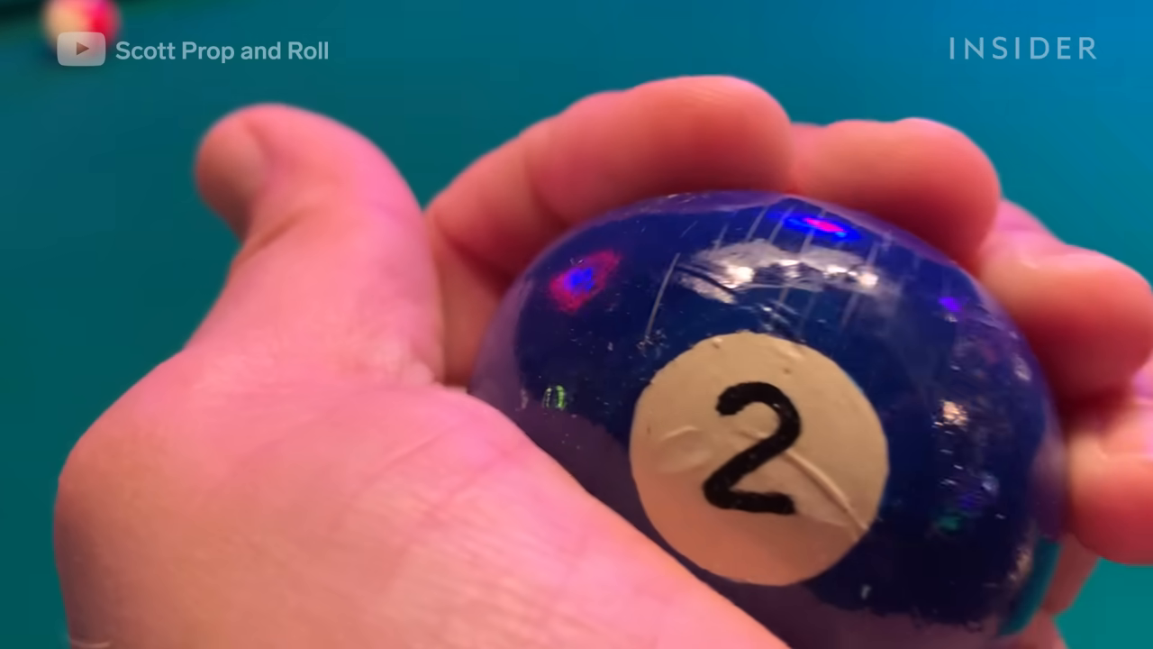 A close-up showing a property master holding a blue, glossy fake pool ball (the 2-ball) made from a racquetball.