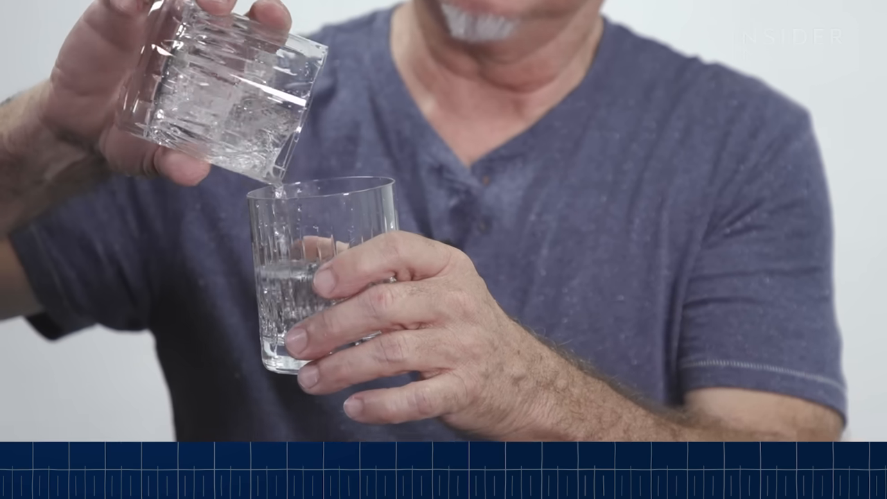 A close-up showing water being poured from a glass over completely silent, jagged silicone prop ice cubes in another glass, accompanied by a flat audio waveform.